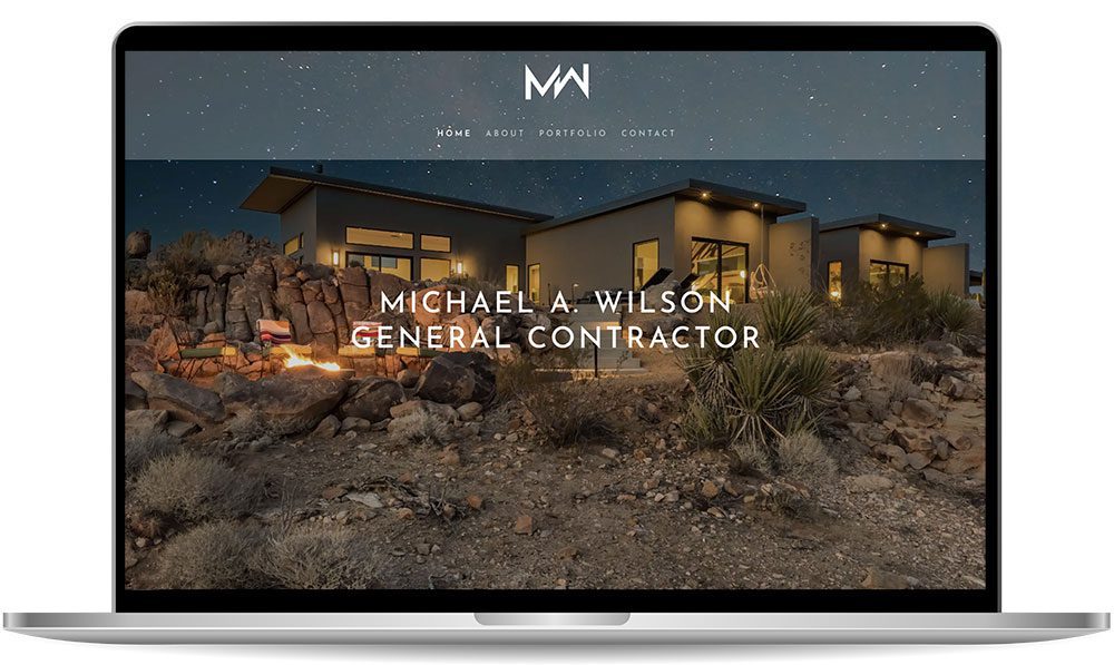 michaelwilson A laptop screen displaying a website for Michael A. Wilson, General Contractor, featuring a modern house at dusk in a rocky, desert landscape.