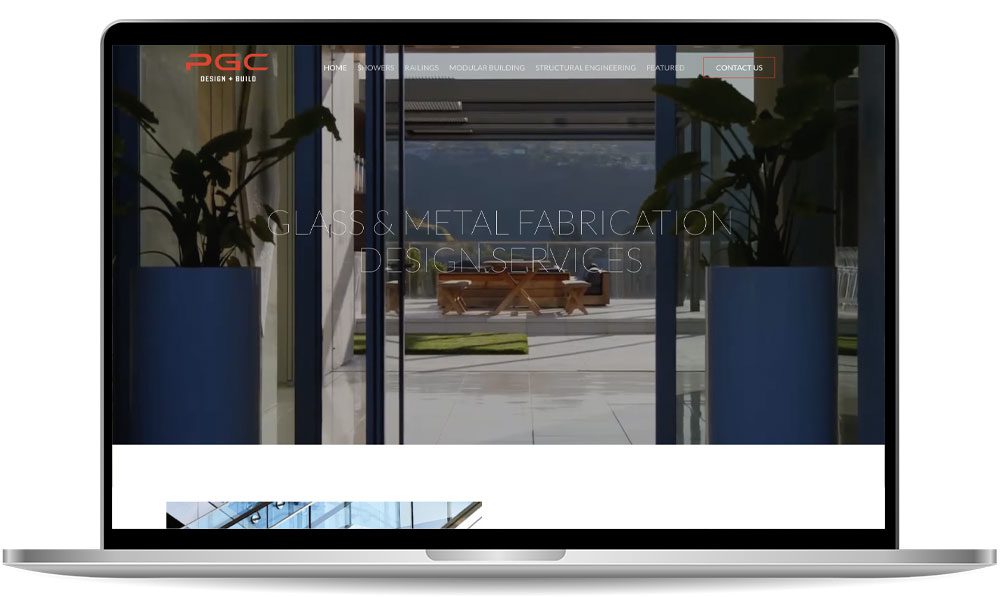 Laptop screen displaying a website for a design and build company specializing in glass and metal fabrication, showcasing a modern building interior through glass doors.