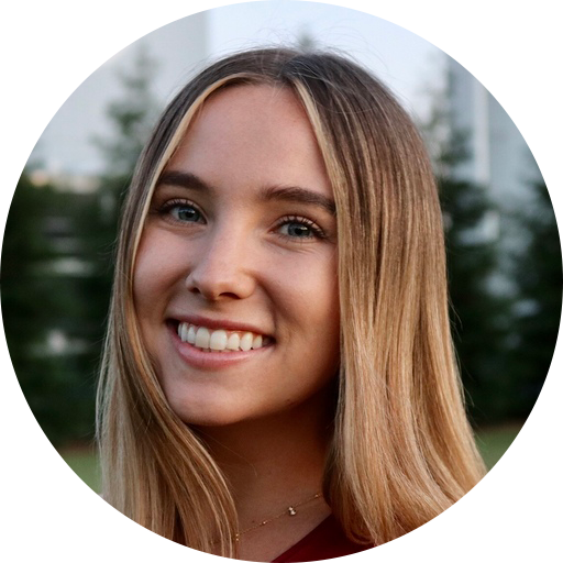 headshots-taylor Woman with long blonde hair smiling, outdoors with trees and a building in the background.